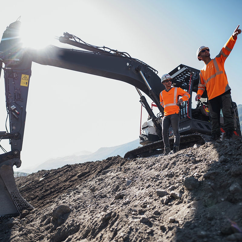 Deux collaborateurs à côté d'une pelleteuse - Crédit photo : ©Atypix